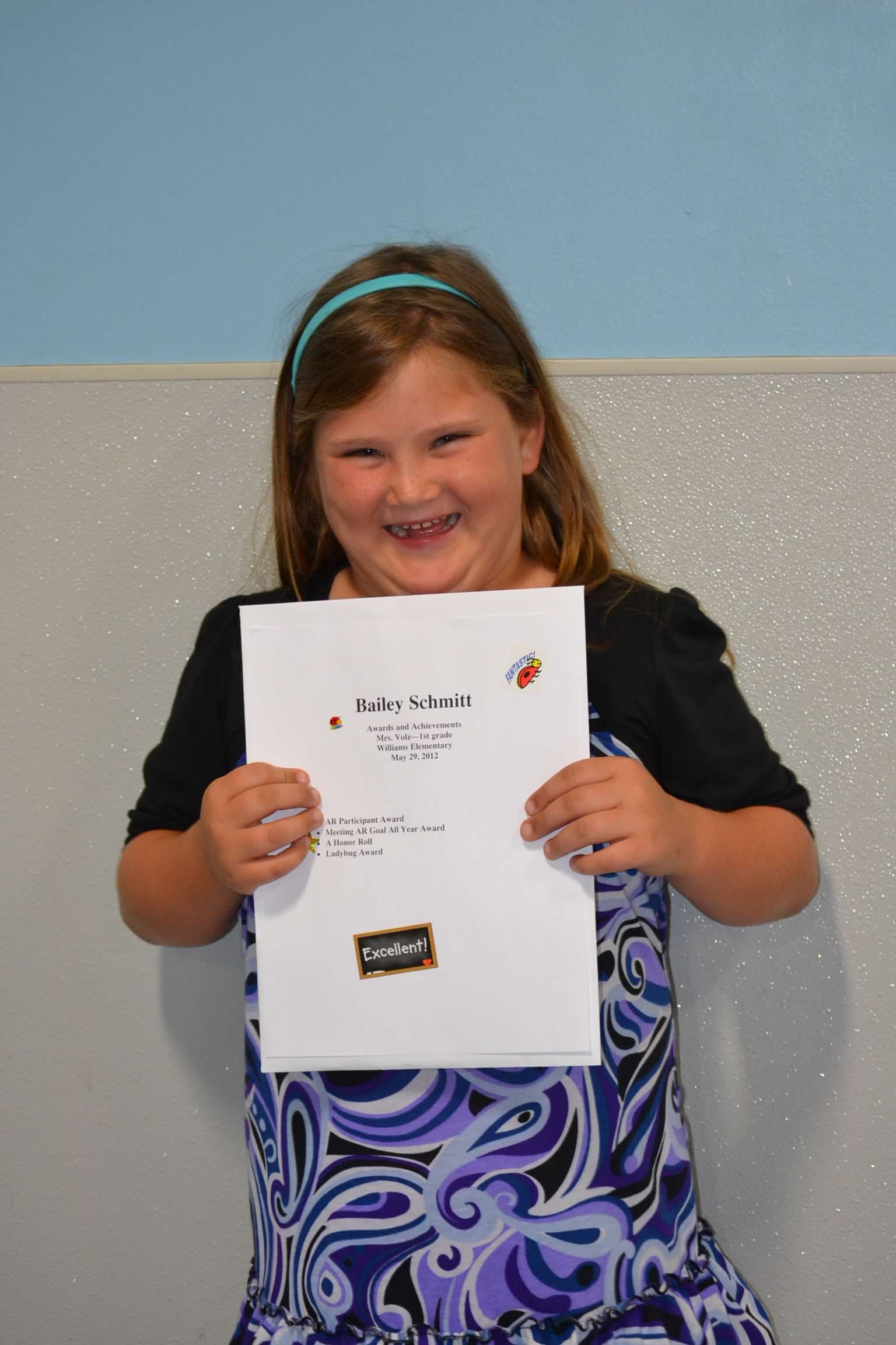 Bailey Schmitt smiling and holding an awards certificate from her elementary school