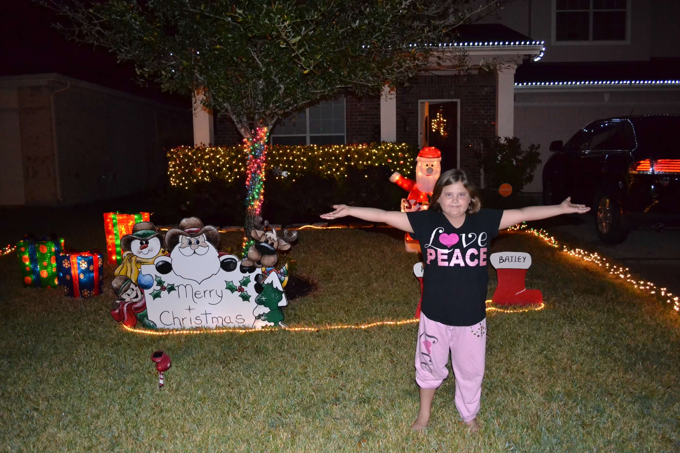 Bailey Schmitt standing outside at night with her arms wide, surrounded by Christmas lights and yard decorations