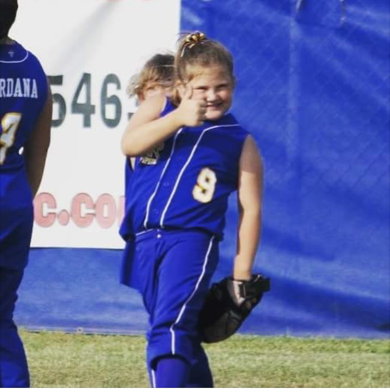 Bailey Schmitt in her #9 softball uniform, giving a thumbs up to the camera