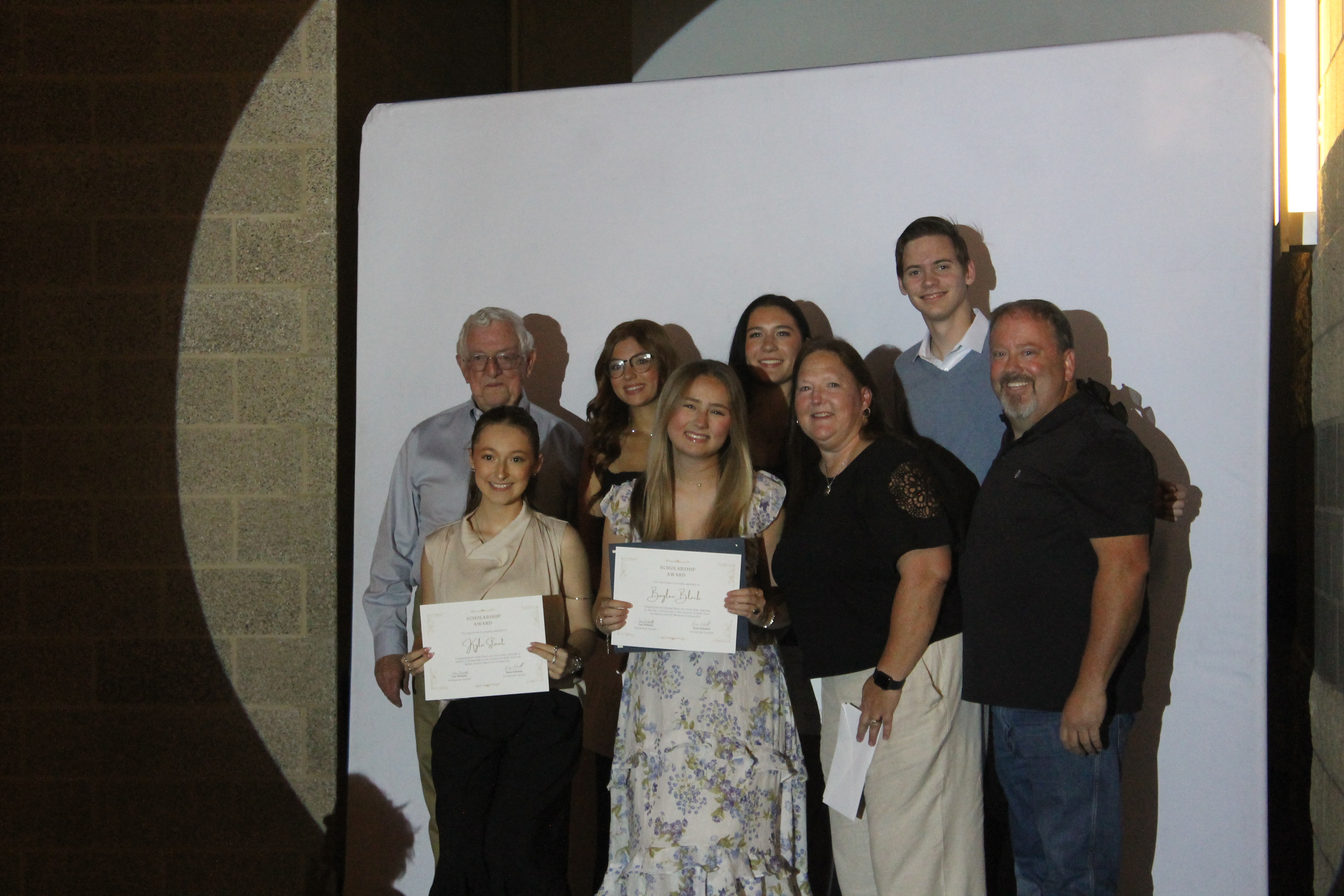 Two of the five Bailey Schmitt Memorial Fund scholarship recipients holding certificates with Len and family at the Needville High School awards ceremony