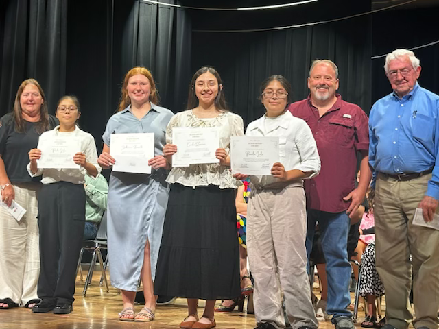 Four Bailey Schmitt Memorial Fund scholarship recipients holding certificates with Len and family at the Palacios High School awards ceremony