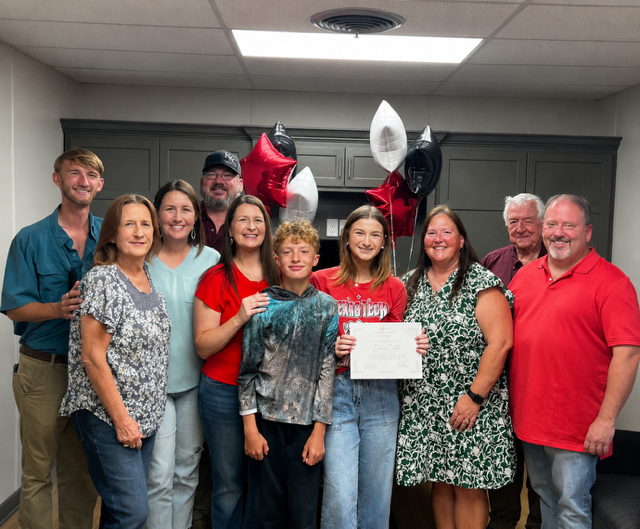 A Bailey Schmitt Memorial Fund scholarship recipient wearing a Texas Tech shirt and holding her certificate at an indoor ceremony with family and balloons